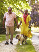 Mature couple walking their dog together on a tree-lined path, enjoying an active lifestyle outdoors